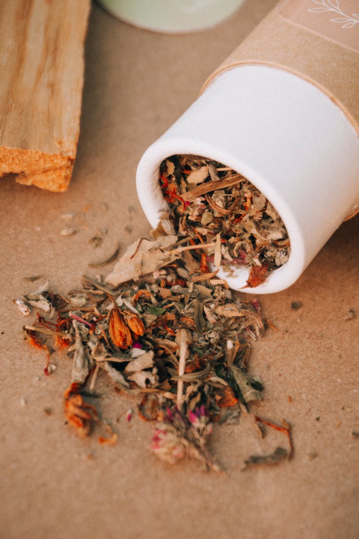 A close-up of dried herbs spilling from a cardboard tube in a natural setting.