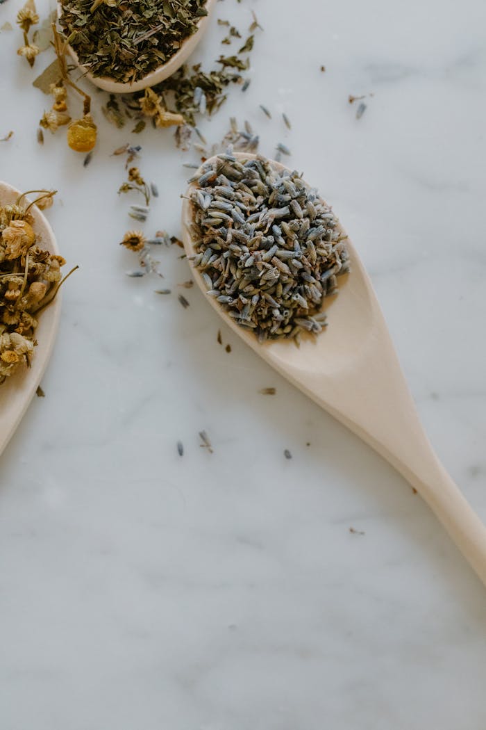 Close-up of dried lavender and chamomile on wooden spoons, showcasing natural remedies.